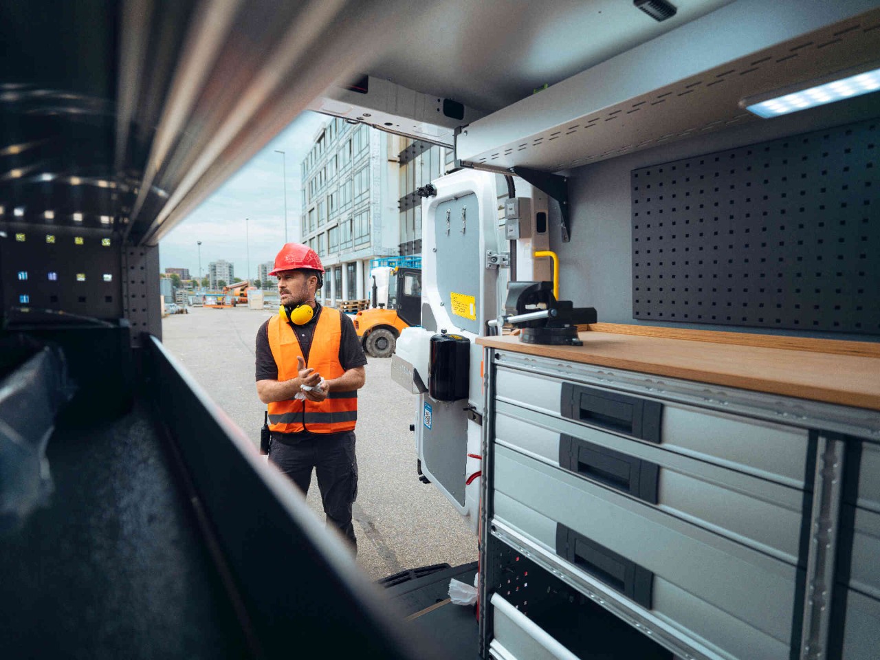 Interieur van een werkvoertuig met werkbank en bouwvakker op de achtergrond.