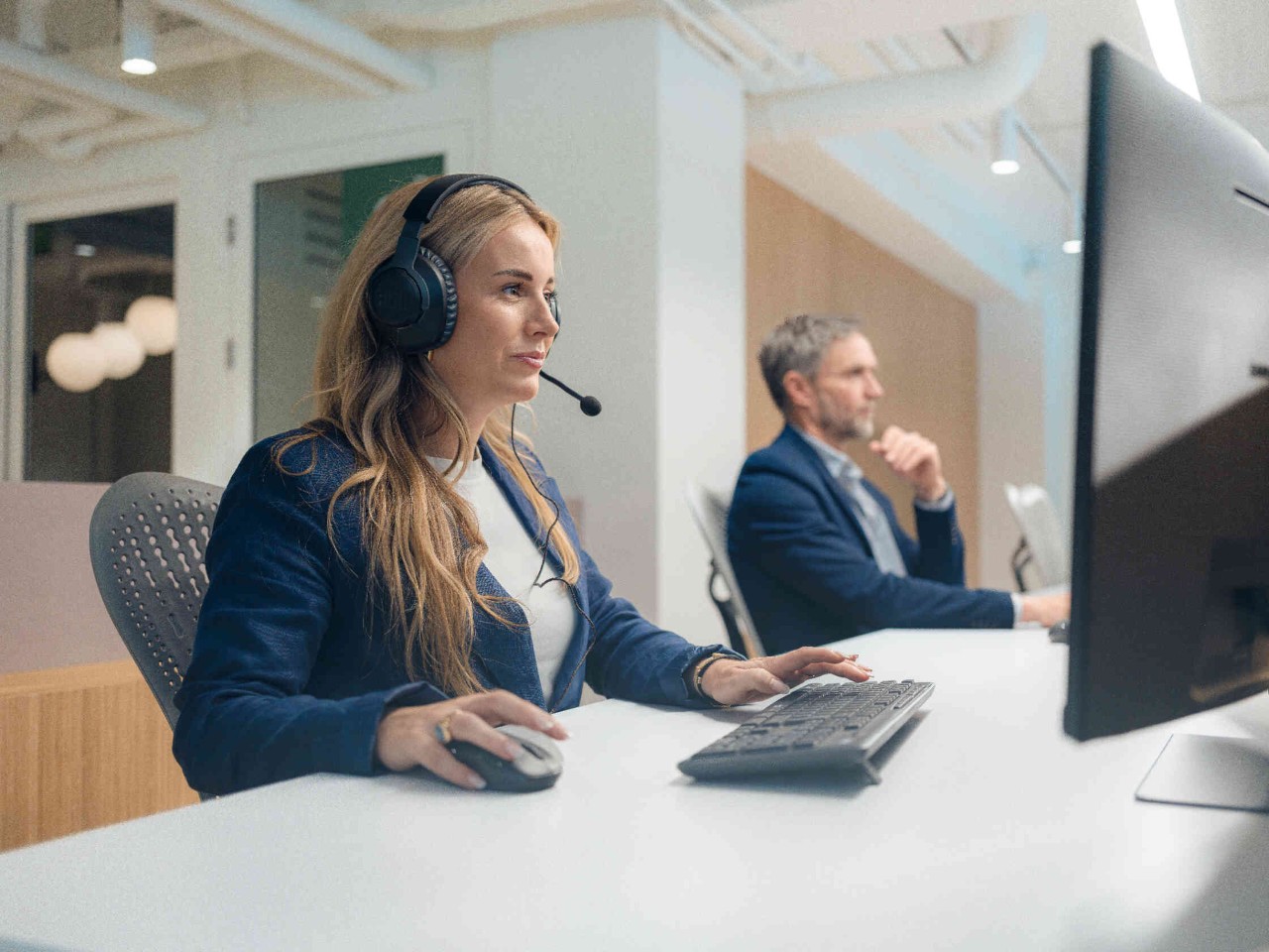 Vrouw met headset aan de monitor man in pak geconcentreerd moderne kantooromgeving.