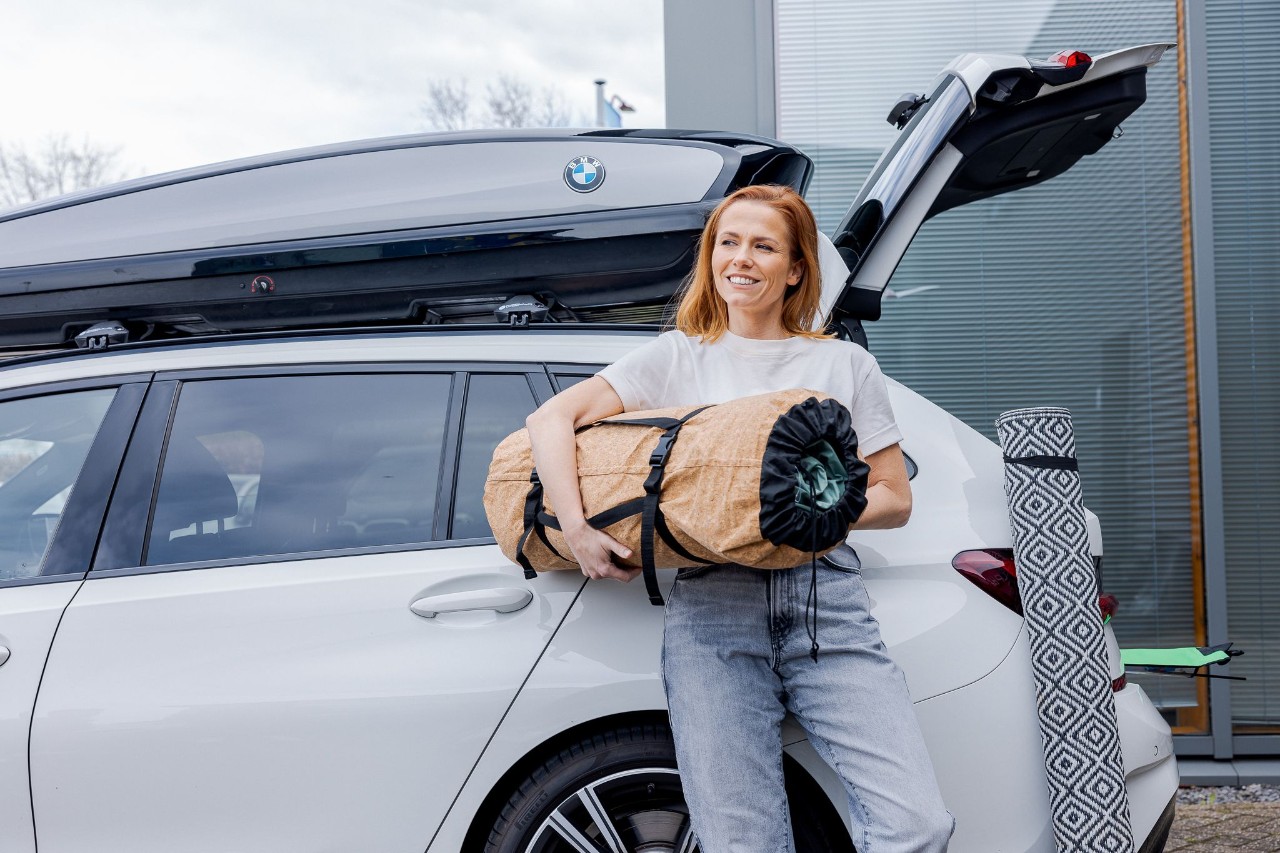 Vrouw leunt tegen haar auto om straks op vakantie te gaan.