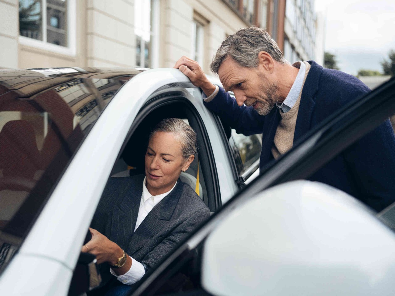 Man leunt op het dak van een witte auto en spreekt met de vrouw op de bestuurdersstoel.
