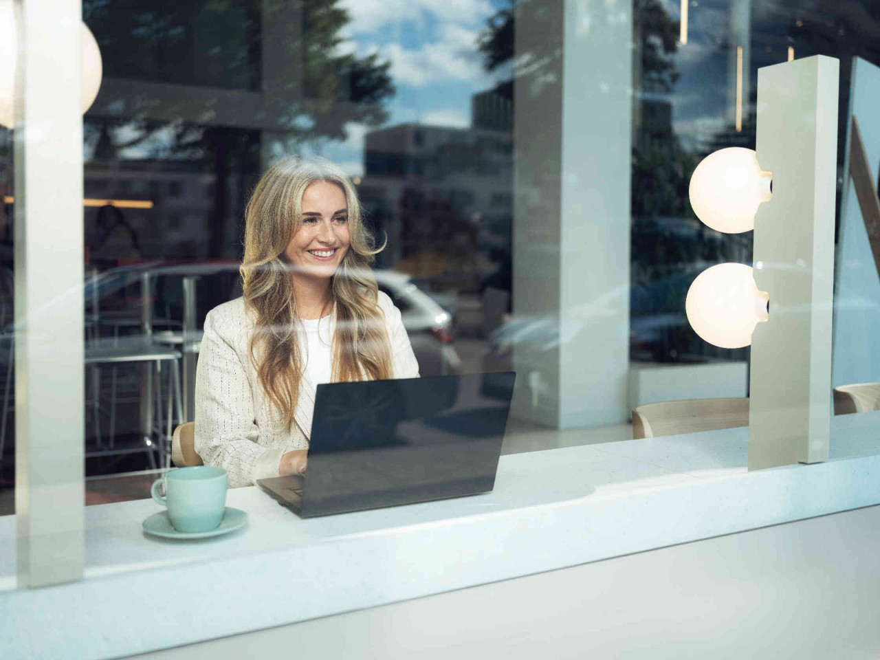 Vrouw in modern caf? werkt op laptop elegante outfit en turquoise kopje en glimlacht.