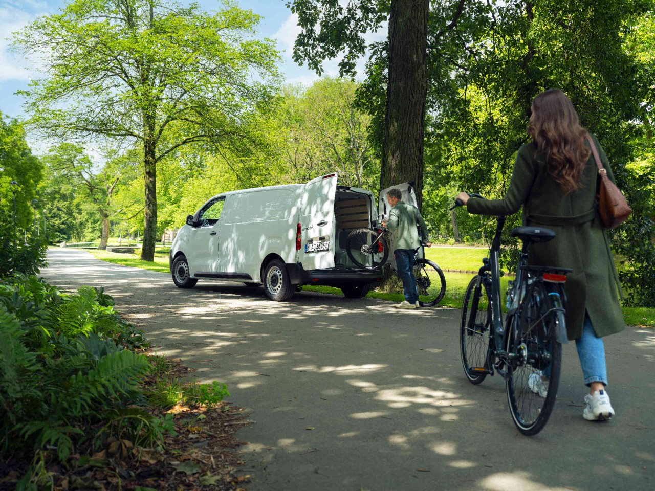 Vrouw duwt een fiets in het park man laadt op de achtergrond een fiets in de transporter.
