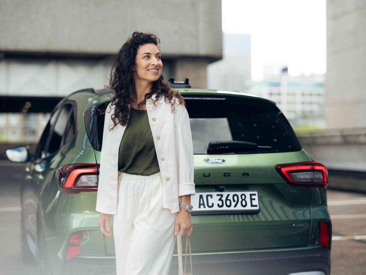 Vrouw in witte outfit voor groene Ford stedelijke ambiance met moderne gebouwen.