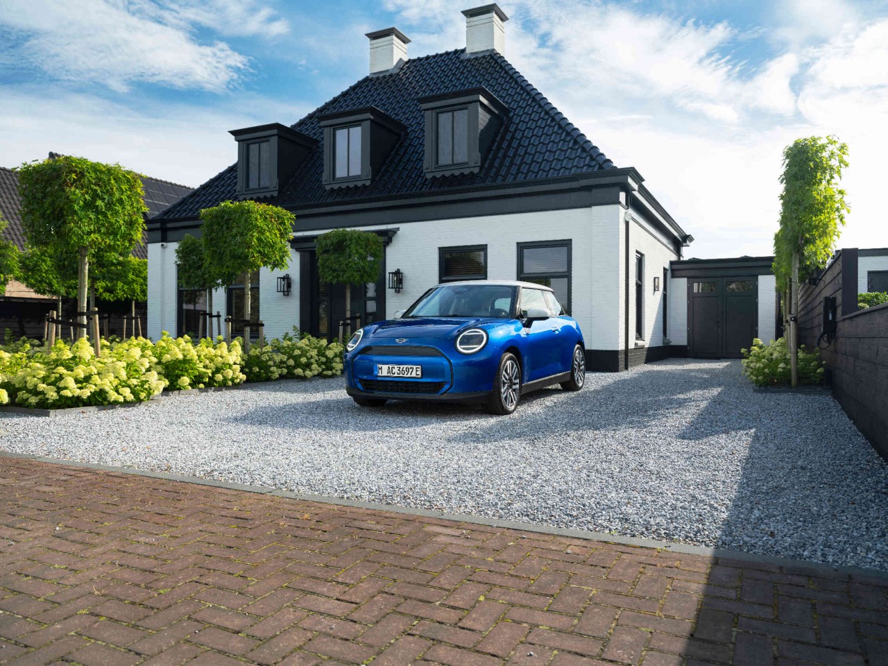 Blauwe MINI-auto staat op een grindoprit voor een woonhuis.