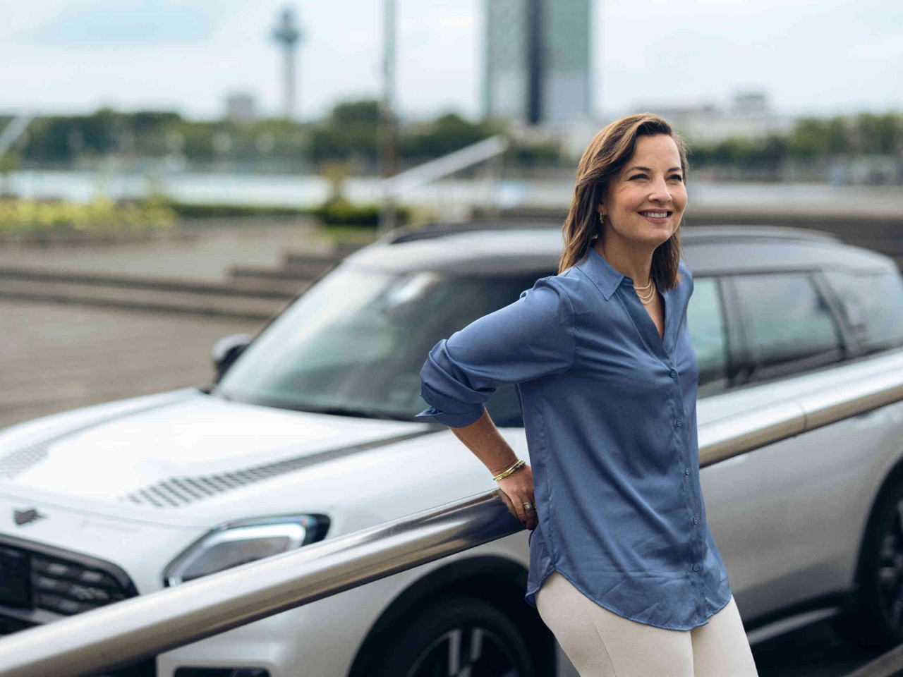 Vrouw leunt tegen een leuning achtergrond toont een witte MINI-auto.
