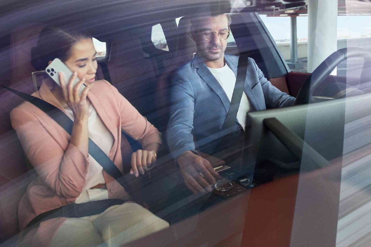 Man en vrouw voor in de auto, de man zit aan de knoppen en de vrouw is aan het bellen met haar mobiel
