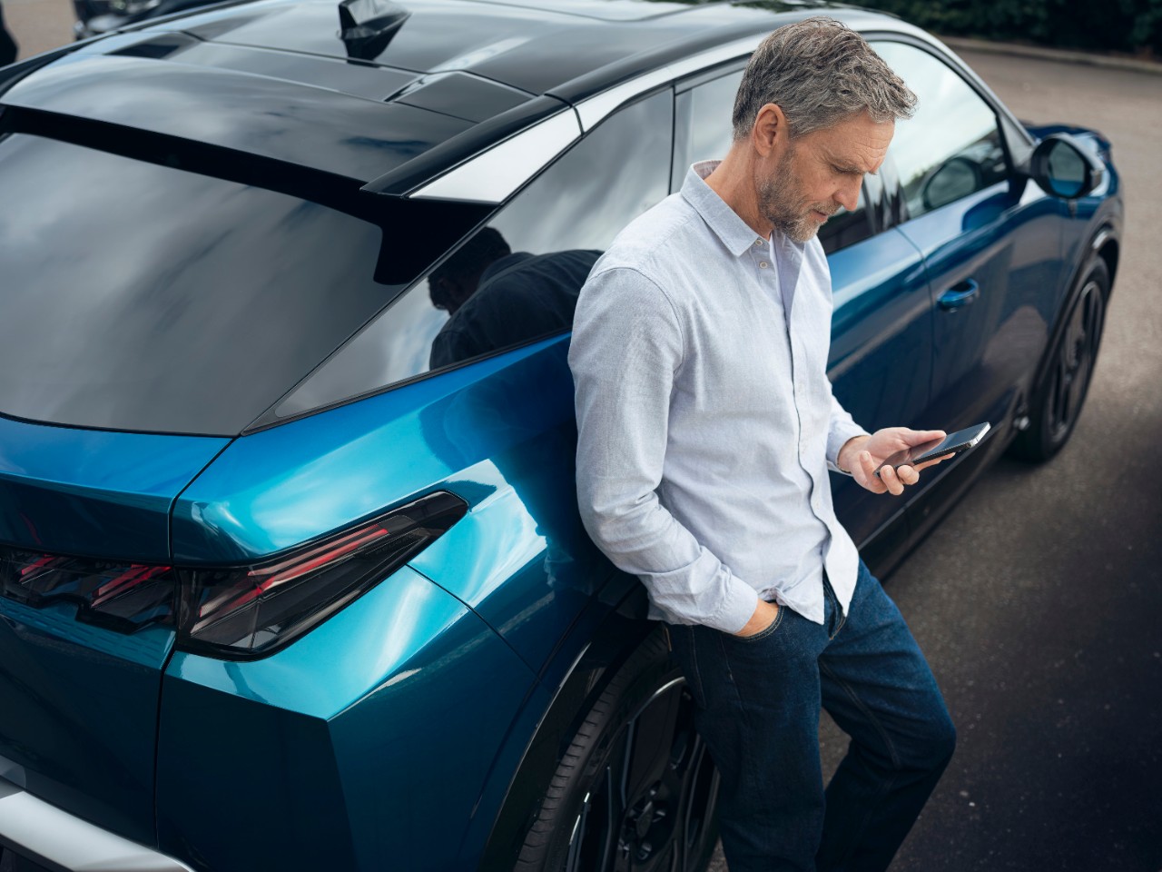 Mann sitzt auf Fahrersitz eines stehendes Autos schaut auf sein Handy Fahrertuer steht offen.