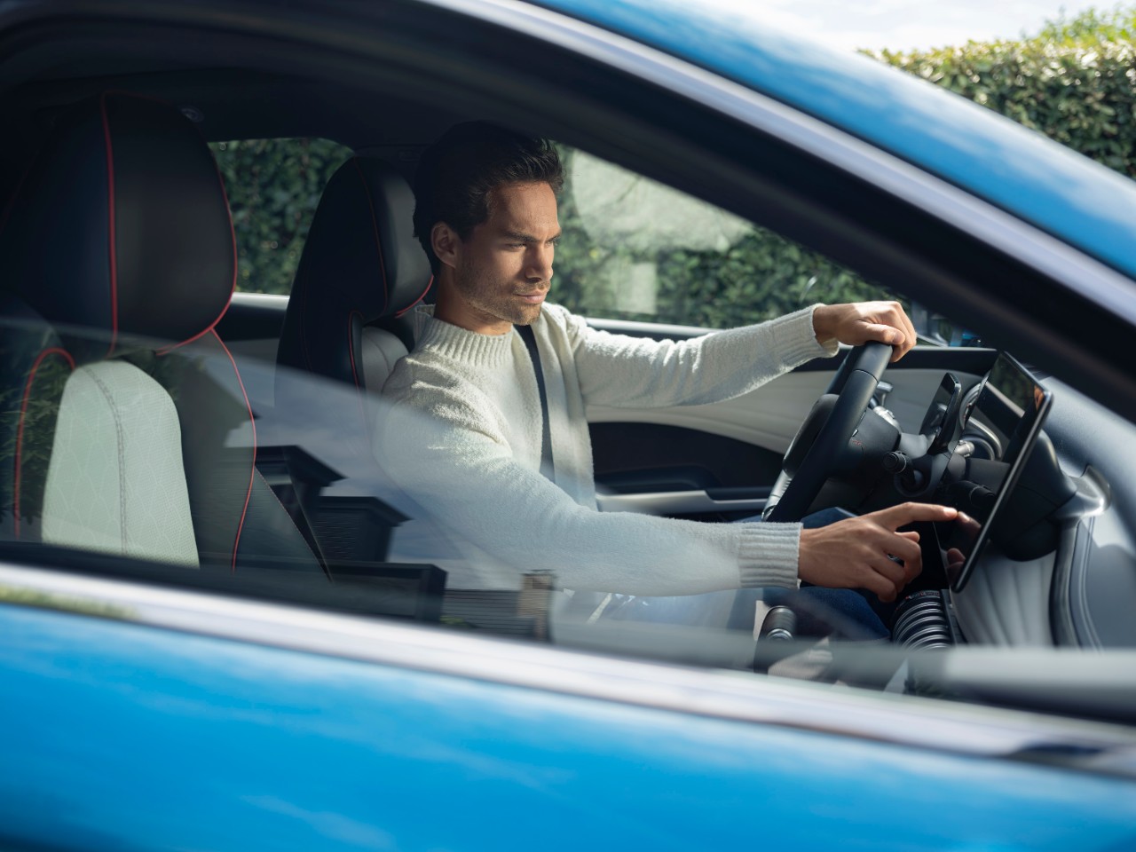 Mann sitzt auf Fahrersitz eines stehendes Autos schaut auf sein Handy Fahrertuer steht offen.