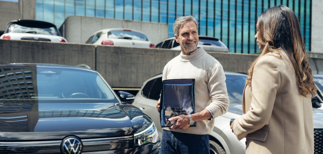 Two people stand next to a Volkswagen.